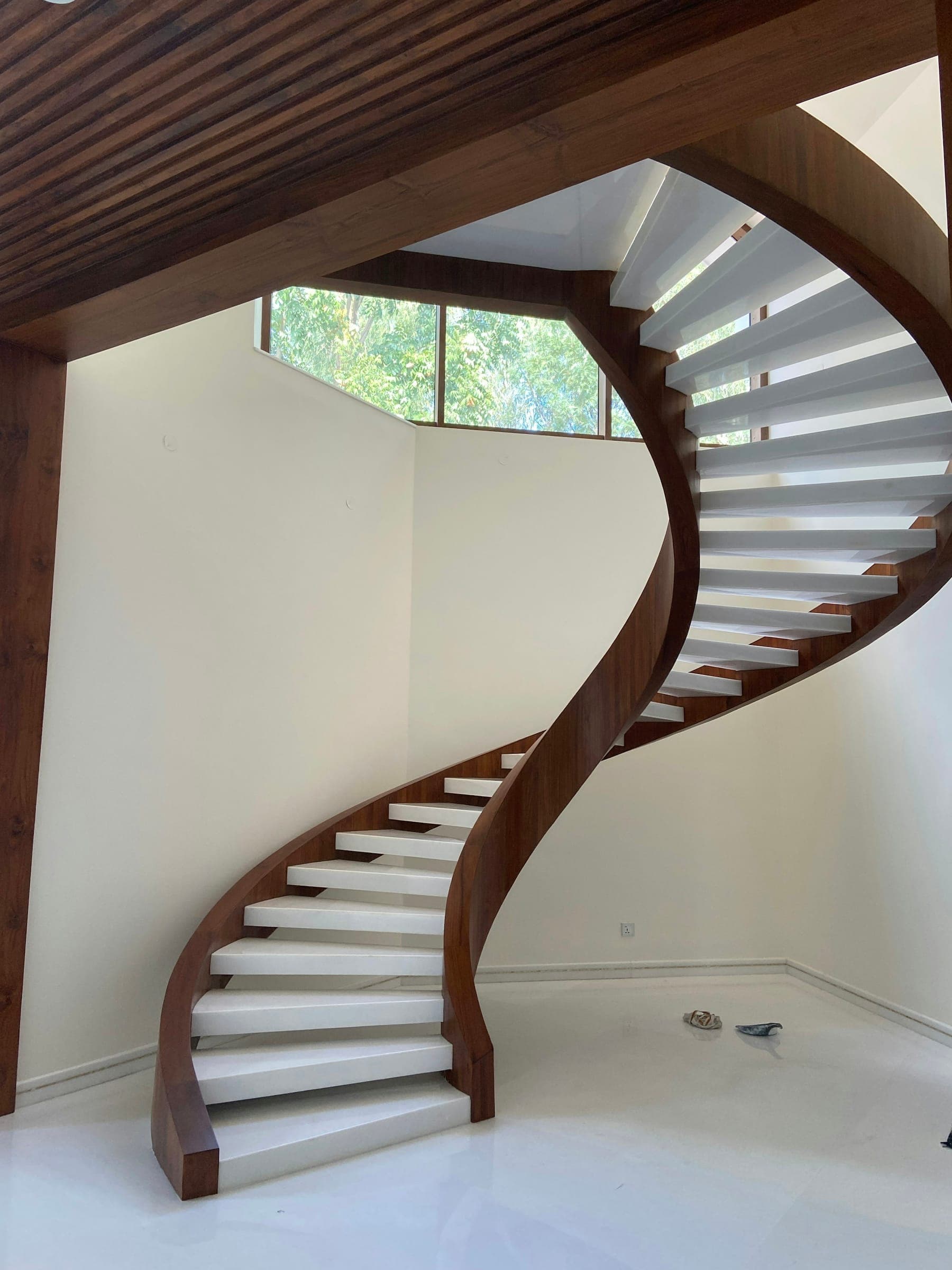 Walnut spiral staircase with white treads against a plaster wall