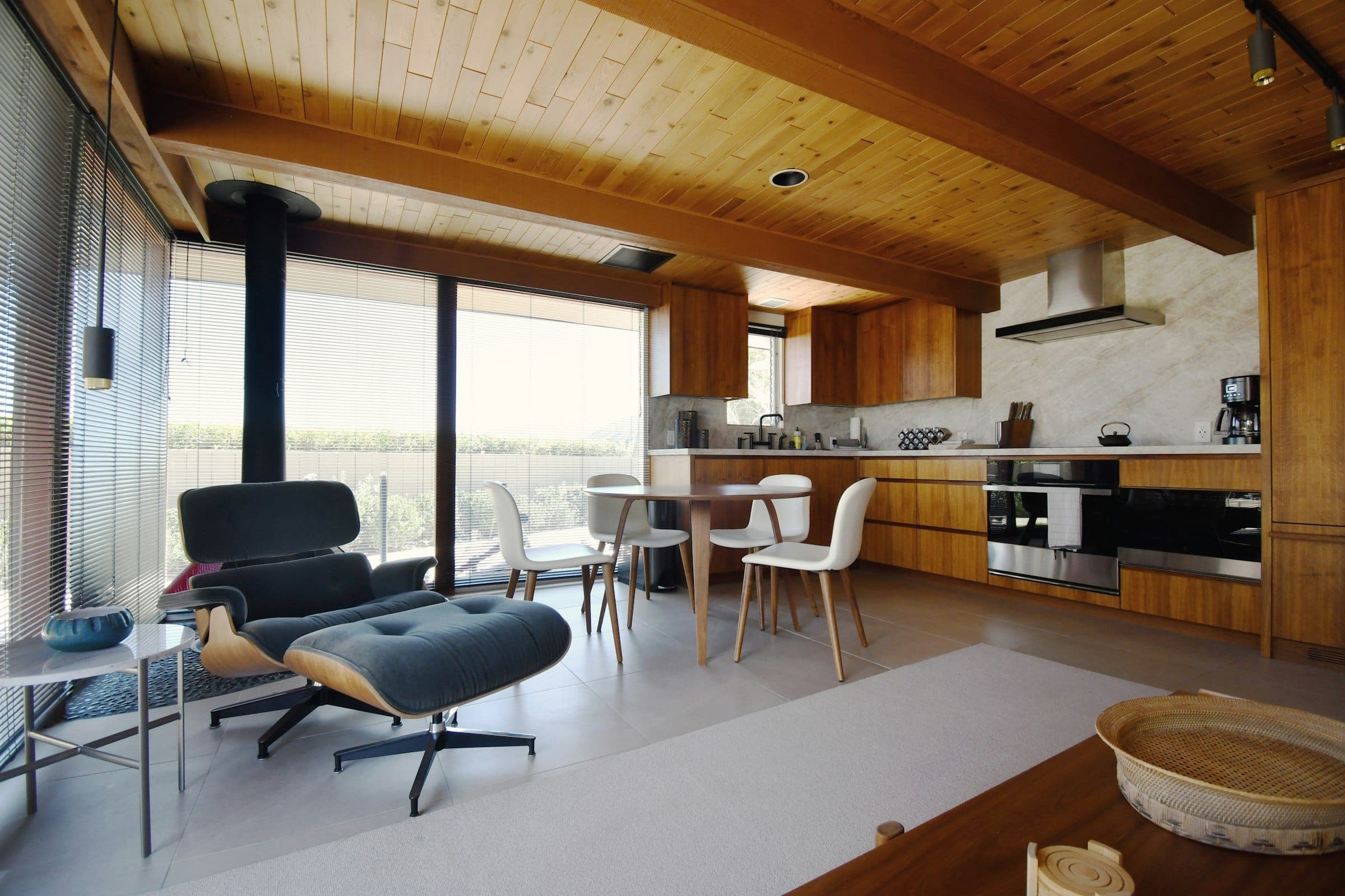 Living room under a sloped wood ceiling with a black stove and tall windows