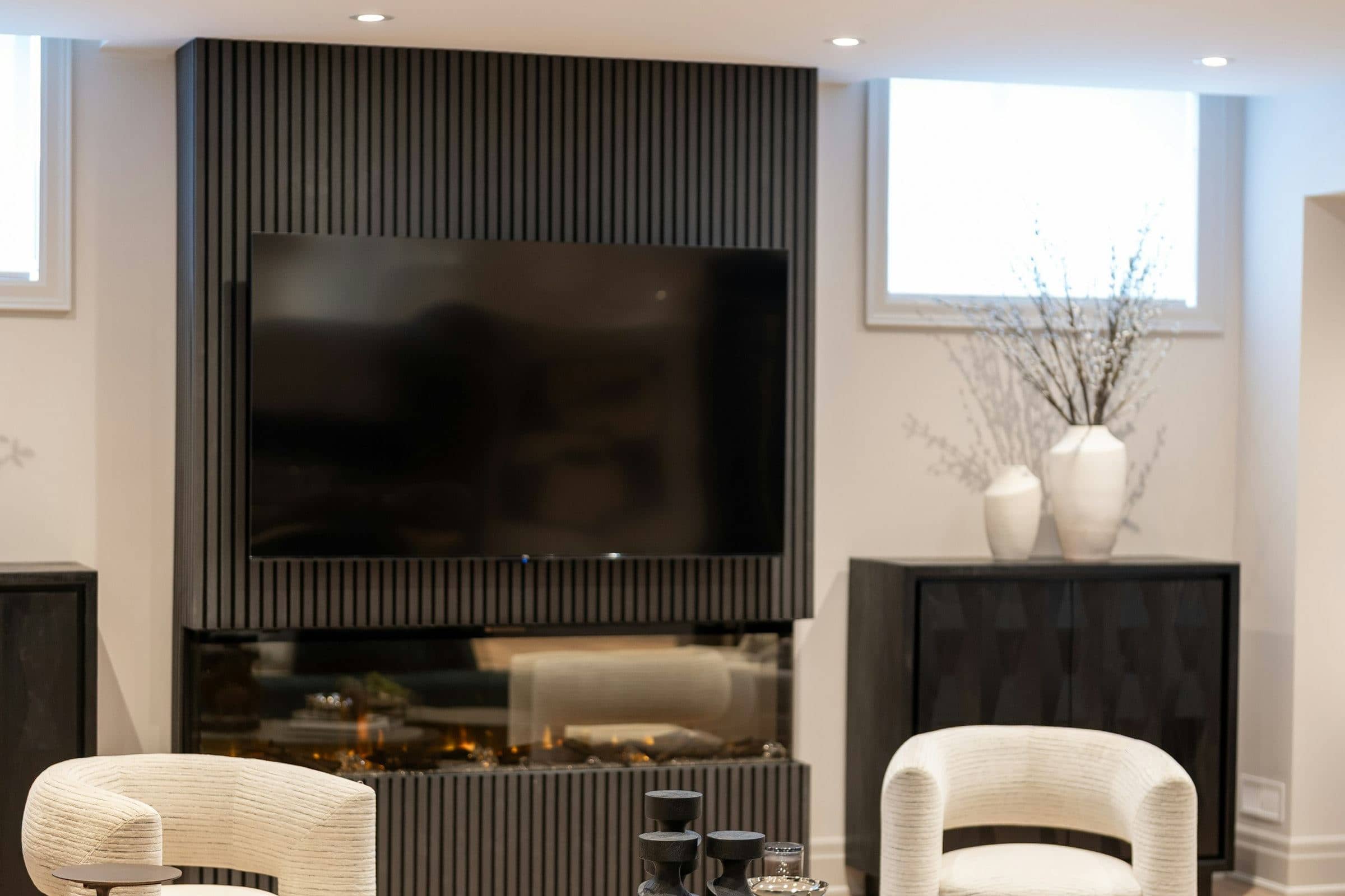 Lower-level family room with a fluted media wall, linear fireplace and daylight windows